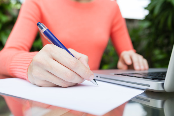 Woman sitting next to a laptop writing